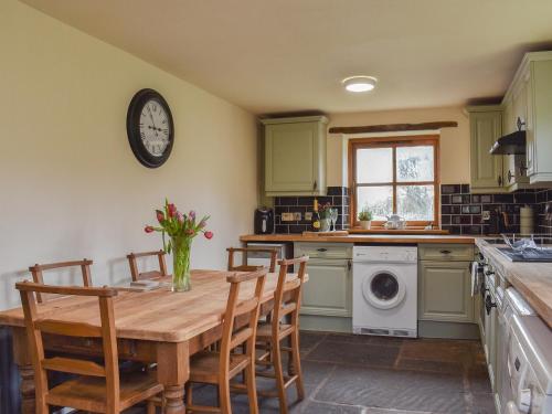 een keuken met een houten tafel en een klok aan de muur bij Beck Foot Cottage in Sedbergh