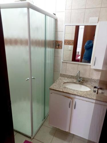 a bathroom with a shower and a sink and a mirror at Apto Pé na Areia com Vista Mar, Churrasqueira e Espaço para 8 Pessoas in Praia Grande