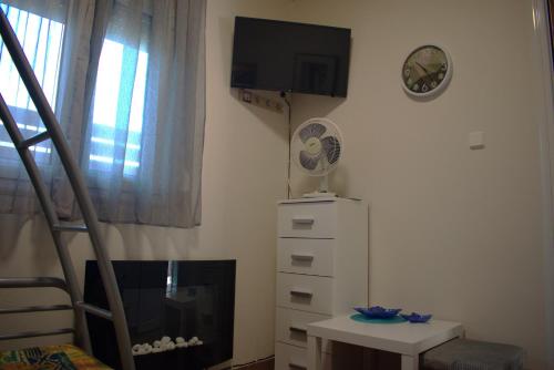 a room with a tv and a dresser and a clock at Verde Home in Néa Meságkala