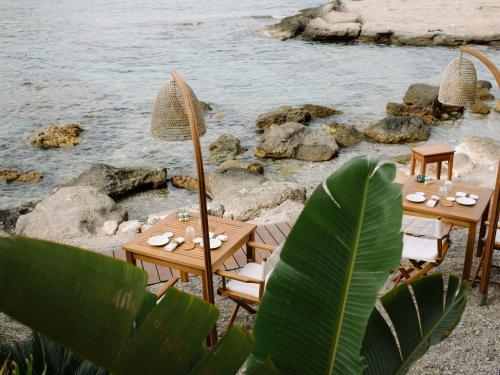 two wooden tables and chairs next to the water at Villa Sant'Andrea, A Belmond Hotel, Taormina Mare in Taormina