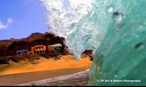a wave crashing on the beach with a house in the background at Rosesplace Mindelo in Mindelo