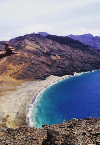 a person sitting on a hill next to a beach at Rosesplace Mindelo in Mindelo