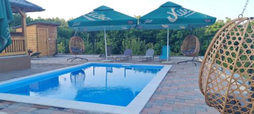 a swimming pool with two umbrellas and chairs and a pool at Vikendica Elenda Banja Luka in Laktaši