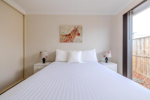 a white bedroom with a large bed and a painting of a zebra at Albany Bayside by the BnB Collection in Albany