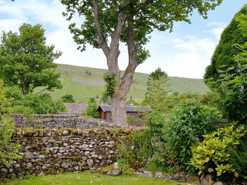 a garden with a stone wall and a tree at Fell View in Kettlewell