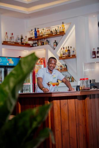 a man standing behind a bar with a drink at La Mama Hotel in Uru