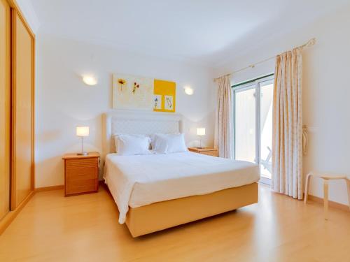 Un dormitorio con una cama blanca y una ventana grande. en 1 bdr apartment with pool next to Laguna Golf Course, en Vilamoura