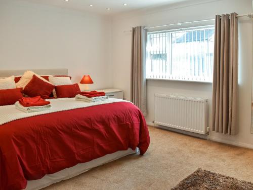 a bedroom with a large red bed and a window at Wylandre in Amlwch