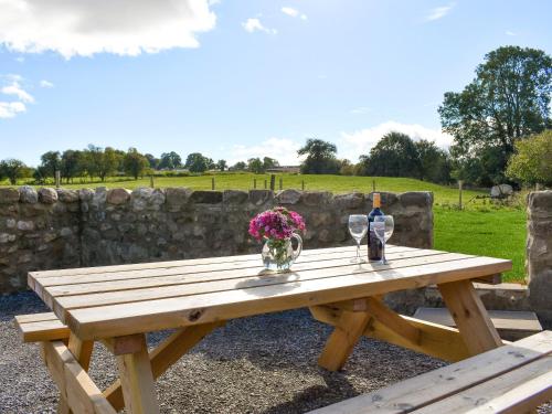 a wooden picnic table with two glasses and flowers on it at Shepherds Den in Crakehall