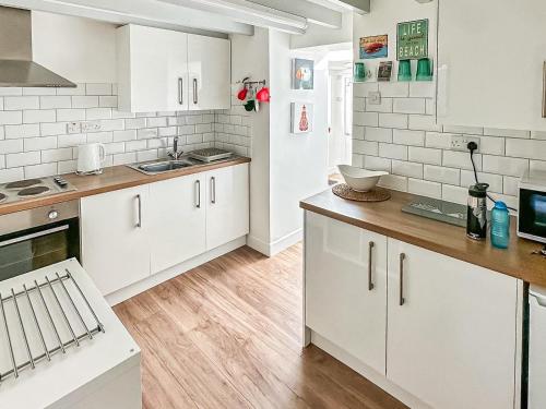 a kitchen with white cabinets and a wooden floor at Seren Cottage By The Sea in Bodorgan