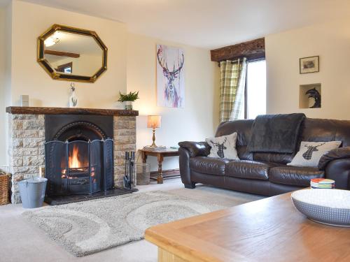a living room with a leather couch and a fireplace at Primrose Bank in Tirril