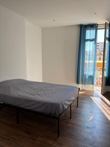 un lit dans une chambre avec une grande fenêtre dans l'établissement T3 rénové Centre historique de Perpignan, à Perpignan