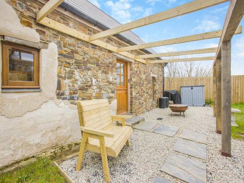 a patio with a wooden bench and a stone building at Olive Barn in Witheridge