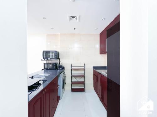a kitchen with red cabinets and a black counter top at 1BR Getaway in RAK l Balcony , Pool and Gym Access in Ras al Khaimah