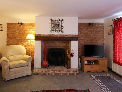 a living room with a fireplace with a chair and a television at Hollyhocks Cottage in Docking