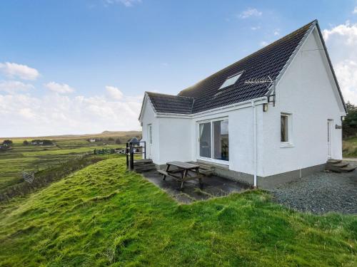 a white house with a picnic table next to a field at Wavecrest in Staffin