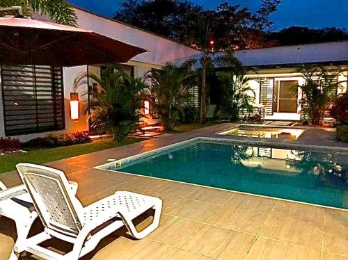 a swimming pool with two chairs and a house at Casa Campestre Ocarros in Villavicencio