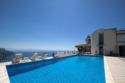 a swimming pool with chairs and the ocean in the background at Hotel Graal in Ravello