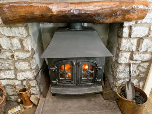 a wood stove in a stone wall with a fire at Oxlow End Cottage in Peak Forest