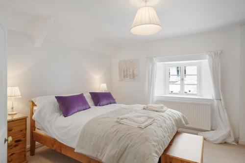 ein Schlafzimmer mit einem Bett mit lila Kissen und einem Fenster in der Unterkunft Historic Cottage & Garden nr Quantock Hills in Nether Stowey