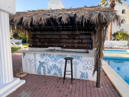 a bar with a straw roof next to a swimming pool at Green Apartment 14 in Tavira Garden in Tavira