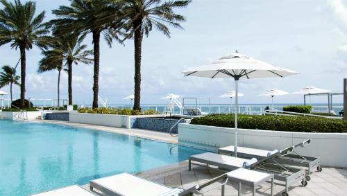 a swimming pool with chairs and an umbrella and palm trees at Beach House Fort Lauderdale, A Hilton Resort in Fort Lauderdale