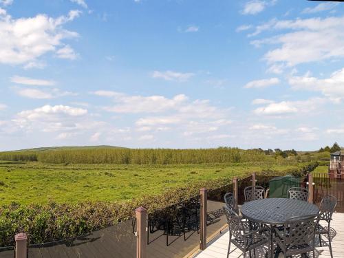 un patio con mesa, sillas y un campo en Meadow View 16, en Ilfracombe