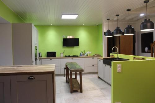 une cuisine avec des murs verts, des armoires blanches et une table dans l'établissement Gîte de Beltaine en Brocéliande SPA et bain nordique, à Mauron