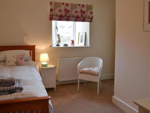 a bedroom with a bed and a chair and a window at Stable Cottage in Chatton