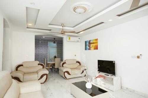 a living room with white furniture and a flat screen tv at Monroe Luxury Apartments in Kumasi