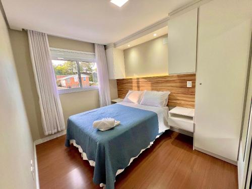 a bedroom with a bed with a blue blanket and a window at Urban Apt 601 Comfortable and Complete in Caxias do Sul