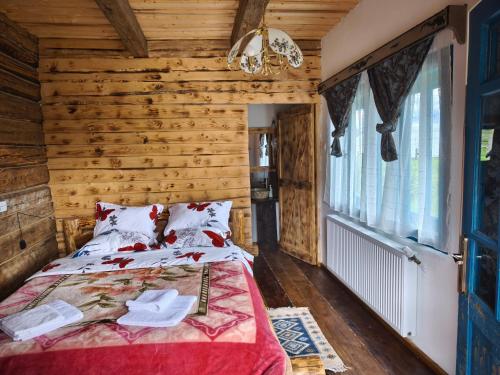a bedroom with wooden walls and a bed with a red bedspread at Căsuța de la munte in Bistriţa