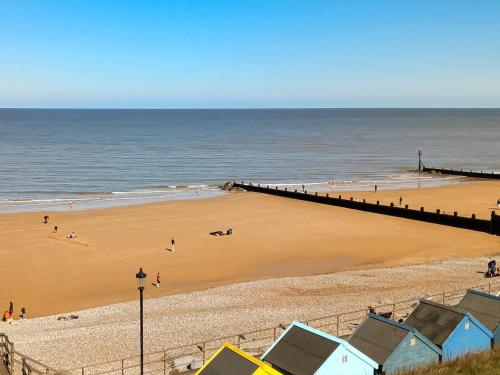 Una playa con gente y un muelle y el océano. en Zero Degrees North, en Sheringham