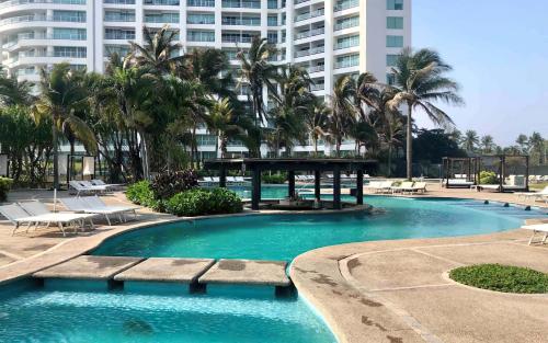 a swimming pool with palm trees and a large building at Departamento Mayan Lakes T6 - Albercas, club de playa, tenis, pádel y más in Acapulco