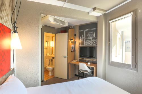 a bedroom with a bed and a desk and a television at Ibis Saint Étienne - La Terrasse in Saint-Étienne