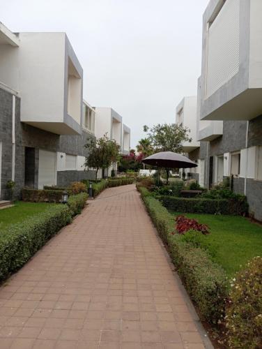 Una pasarela de ladrillos con una sombrilla al lado de un edificio. en Appartement Familial avec Jardin, Résidence avec Piscine Dar El Bahr, en Sidi Rahal