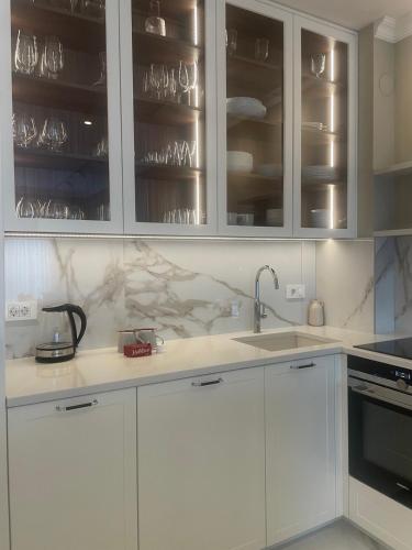 a kitchen with white cabinets and a sink with wine glasses at Apartman Celine PortoNovi in Kumbor