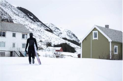 a man walking in the snow carrying a surfboard at Location, location, location in Ervik