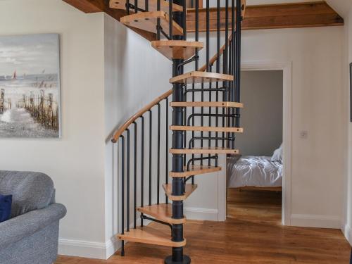 a wooden spiral staircase in a living room at The Old Paybarn - Uk39378 in Snettisham