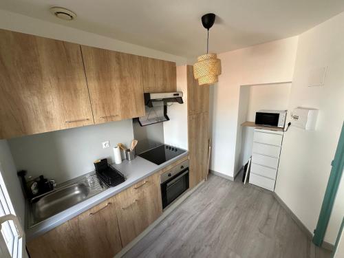 a small kitchen with wooden cabinets and a sink at Appartement rénové et lumineux - 130 in Dax