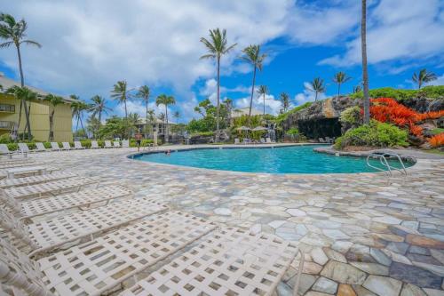 a pool at a resort with chairs and palm trees at Idyllic Yet Simple Oceanfront Resort Stay in Lihue