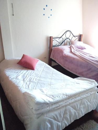 a bedroom with two beds with white sheets and a pink pillow at Casa Hermosa in Quito