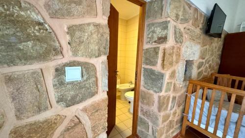 a bathroom with a stone wall with a toilet and a crib at Raízes da Vinha - Quartos & Chalé na Serra da Estrela in Carragozela