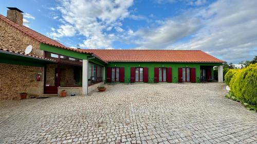 a green building with red doors and a brick driveway at Raízes da Vinha - Quartos & Chalé na Serra da Estrela in Carragozela
