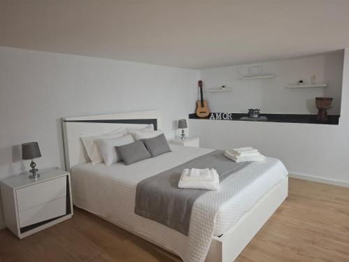 a white bedroom with a large bed and a guitar at Casa do Diniz in Travassos