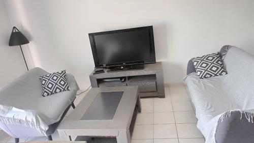 - un salon avec deux chaises et une télévision à écran plat dans l'établissement Le havre des Sables, à Les Sables-dʼOlonne