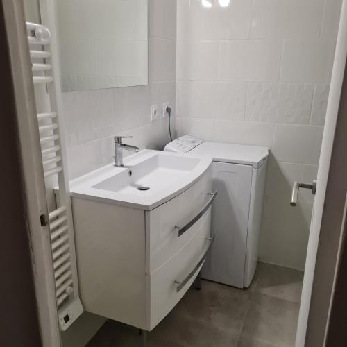 La salle de bains blanche est pourvue d'un lavabo et d'un lave-linge. dans l'établissement Appartement Climatisé Nîmes, à Nîmes