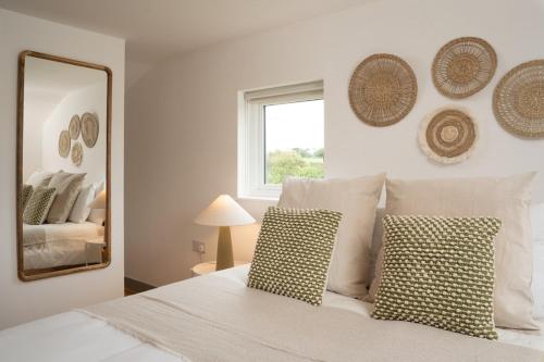 a bedroom with a white bed with pillows and a mirror at Idyllic hideaway with hot tub, gym & gamesroom in Penzance