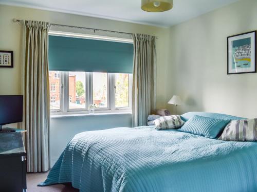 a bedroom with a bed with a blue comforter and a window at Lime Court - Cottages in Leatherhead