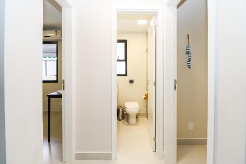 a white bathroom with a toilet and a hallway at Apartamento Garden Caiobá com Piscina Praia Brava in Matinhos